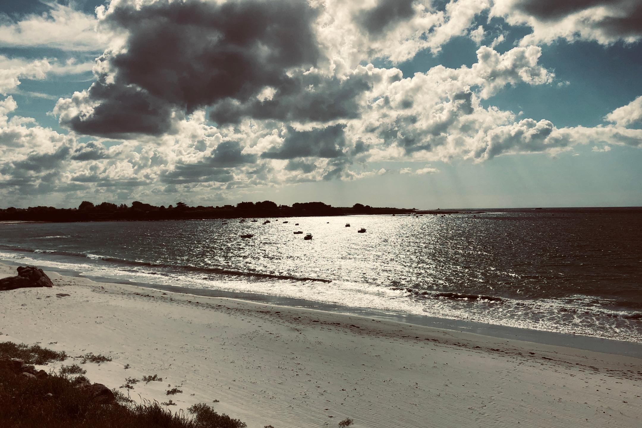 Die Sonne scheint auf einen Strand am Meer mit kleinen Booten auf dem Wasser.