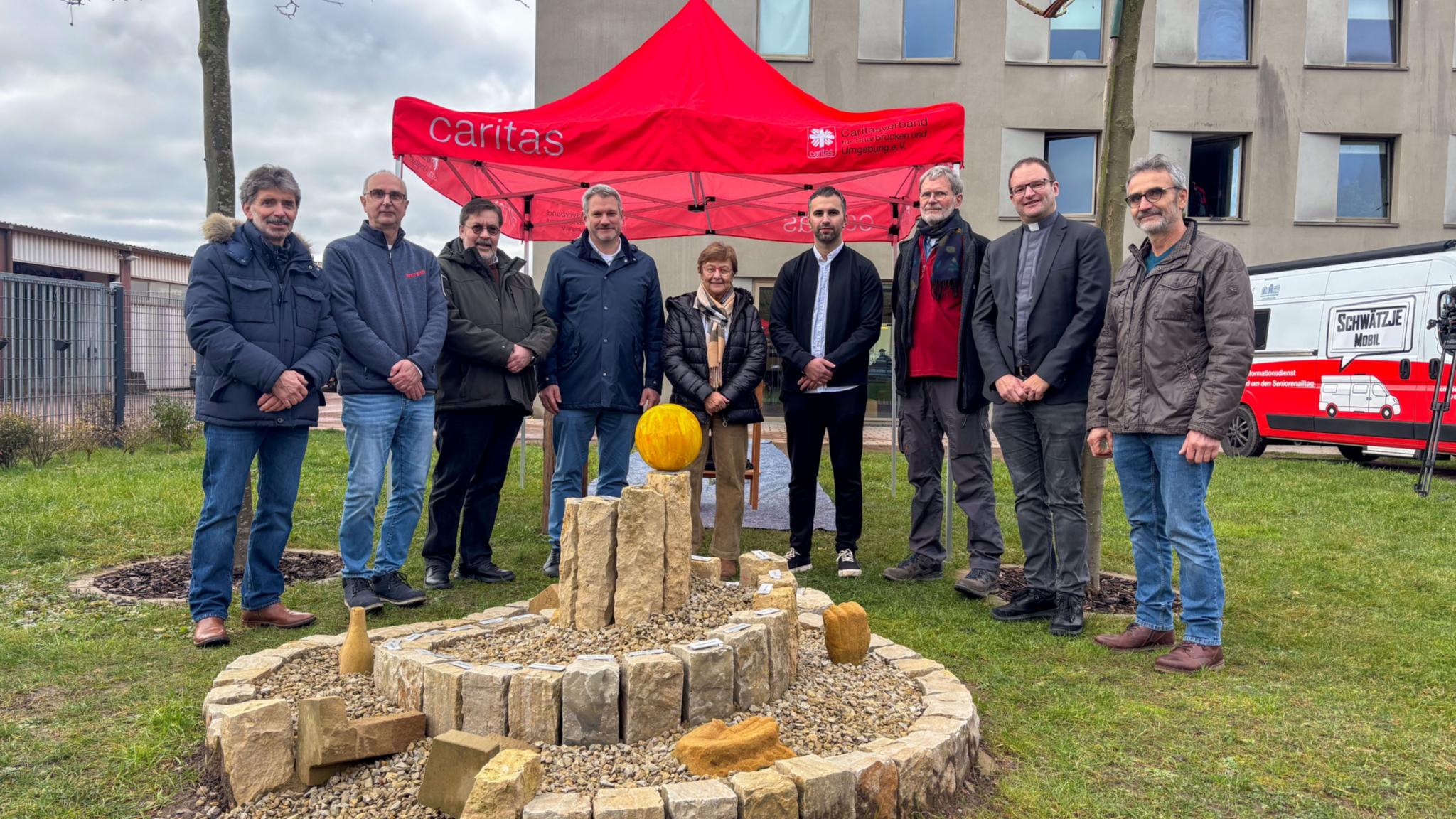 Acht Personen stehen vor einem Zelt der Caritas für ein Gruppenbild zusammen