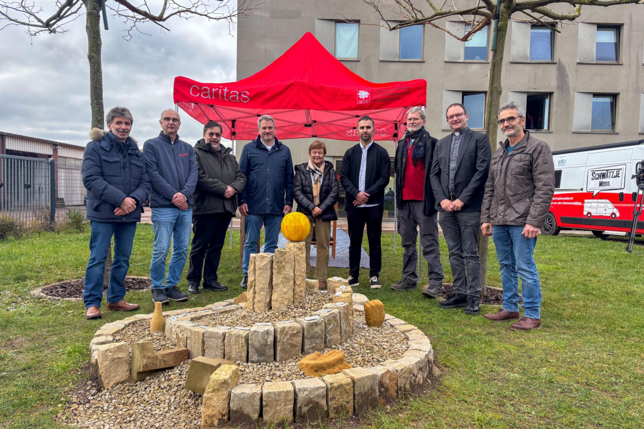 Acht Personen stehen vor einem Zelt der Caritas für ein Gruppenbild zusammen