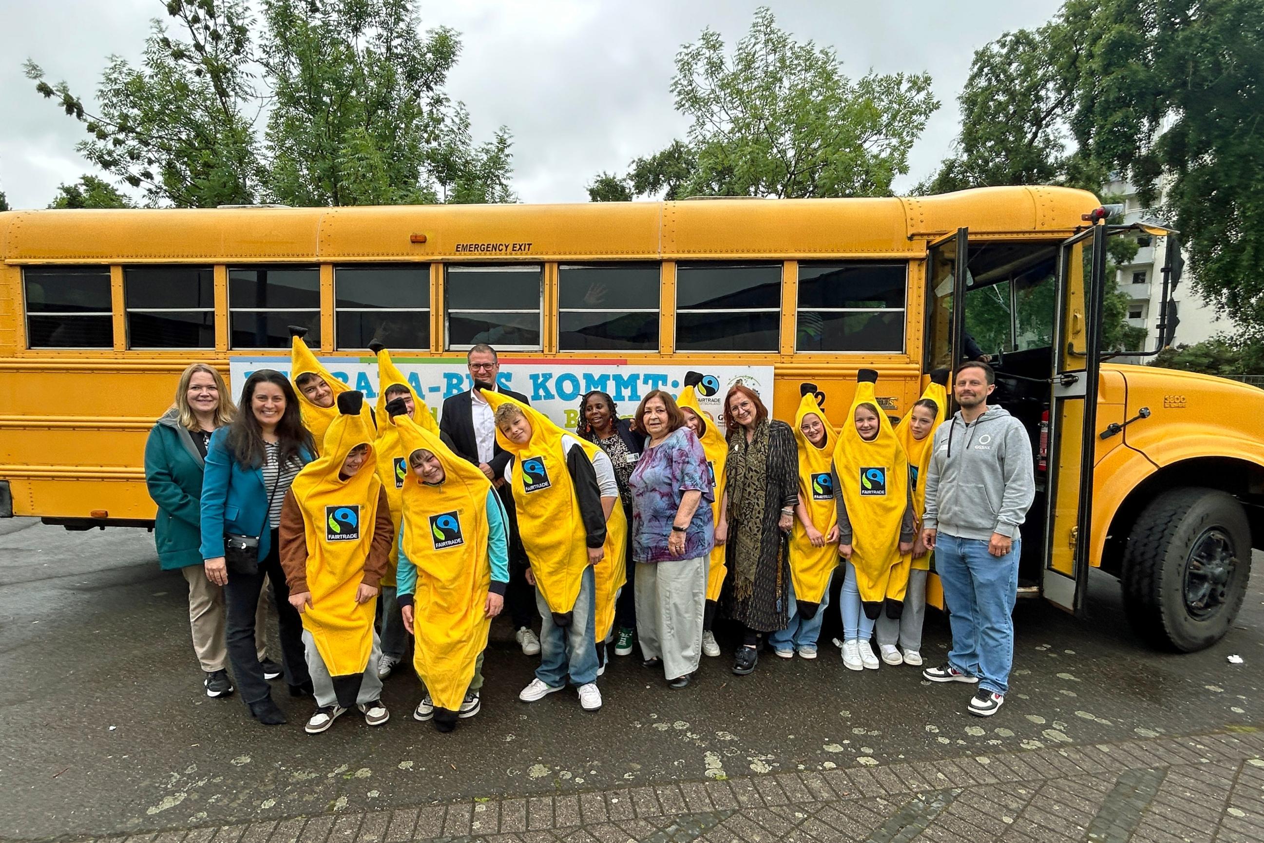 Vor dem Banabus feiern Schülerinnen und Schüler gemeinsam mit Schulleiter Stephan Arnold, Regionalverbandsdirektorin Carolin Lehberger, Bildungsdezernentin Kerstin Theobald und Winnie Mbindyo von Fairtrade Deutschland das zehnte Jubiläum der Willi-Graf-Realschule als Fairtrade-School.