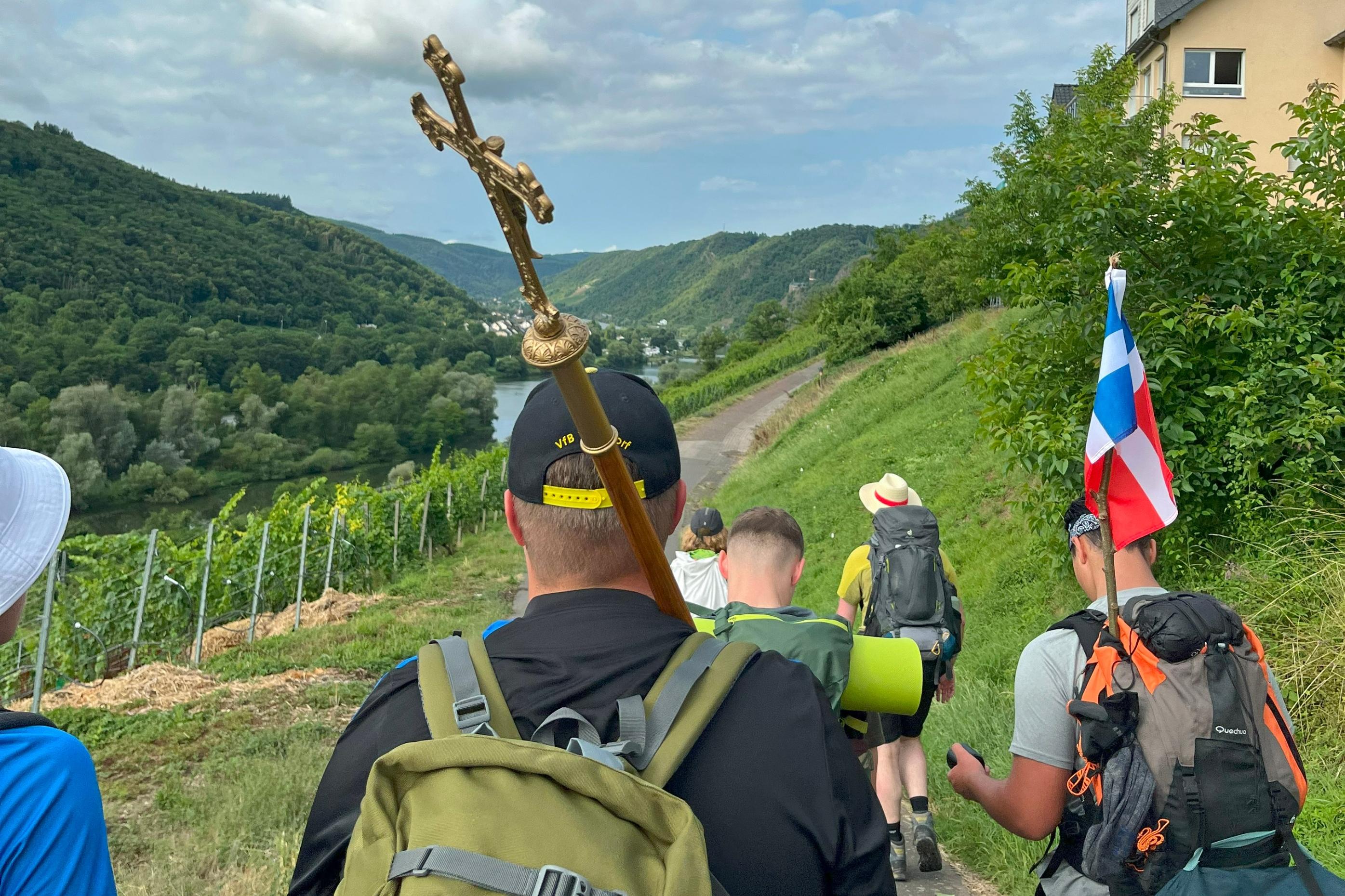 Eine Gruppe junger Menschen pilgert durch Weinberge