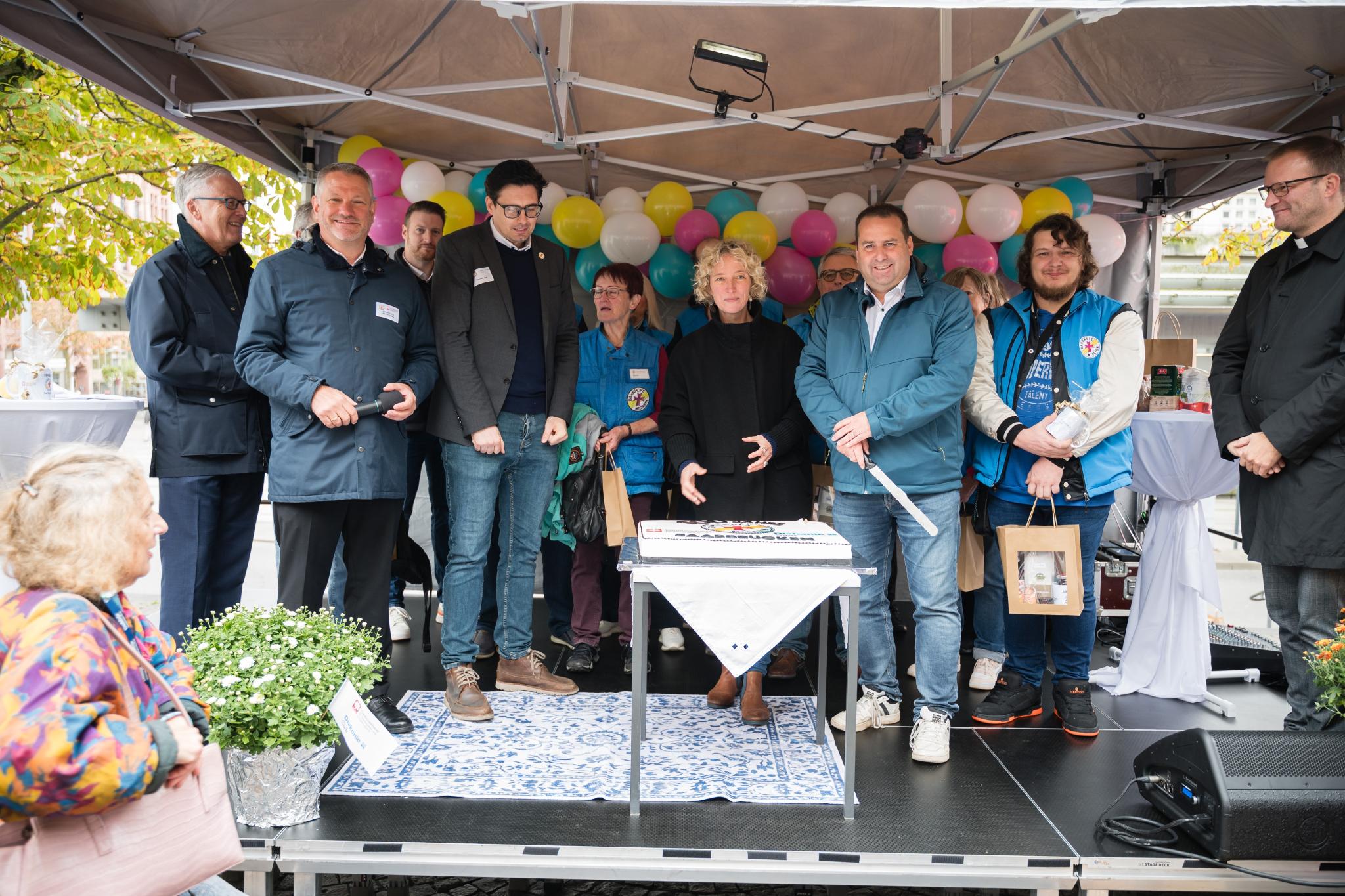 Sozialminister Dr. Magnus Jung (3.v.r.) schnitt mit Jennifer Sauer, Leiterin Bahnhofsmanagement (Mitte), und Tafelkoordinator Thorsten Junk (4.v.l.) die Torte an. Es feierten mit (v.l.n.r.): Dr. Klaus Vornhusen (Deutsche Bahn), Caritasdirektor Michael Schley und Tobias Raab sowie viele Ehrenamtliche.