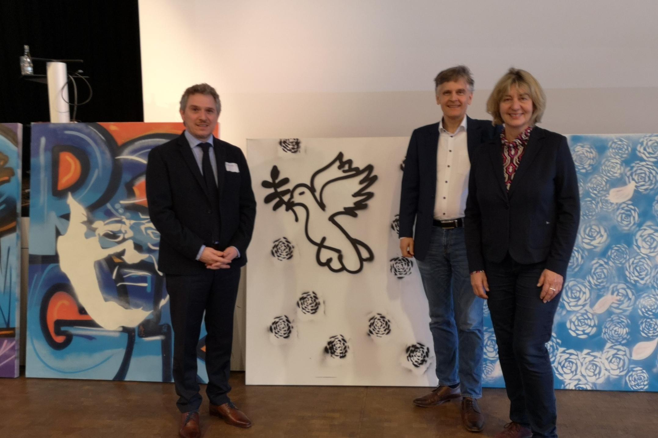 Mit-)Ausrichter PD Dr. Alexander Maier (Fachrichtung Kath. Theologie) und Prof. Dr. Karlo Meyer (Fachrichtung Ev. Theologie) mit Referentin Prof. Dr. Elisabeth Naurath (Universität Augsburg), im Hintergrund einige Streetart-Kunstwerke, die in der Kirche der Jugend eli.ja entstanden.